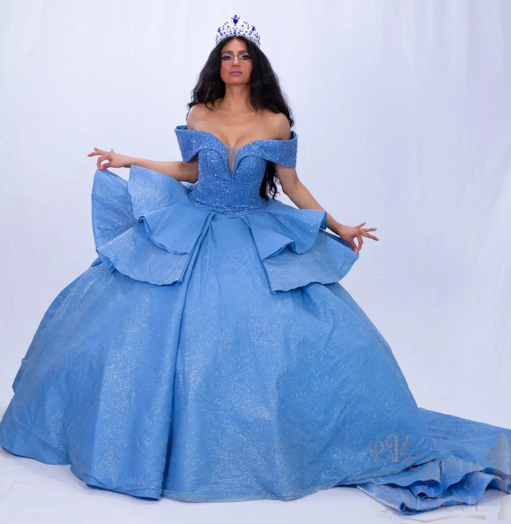 A custom blue quinceañera dress with off-the-shoulder neckline, sweetheart bodice, and ruffled ball gown skirt with a flowing train